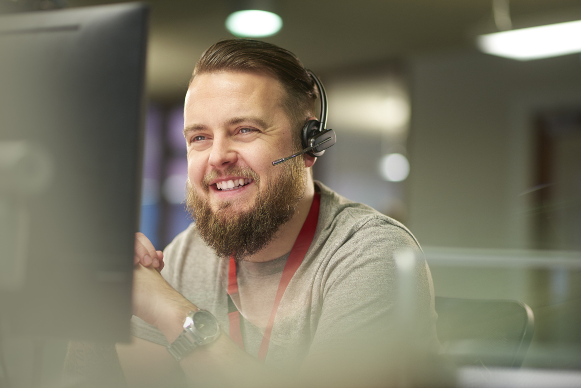 A smiling man speaking with a client via a headset.