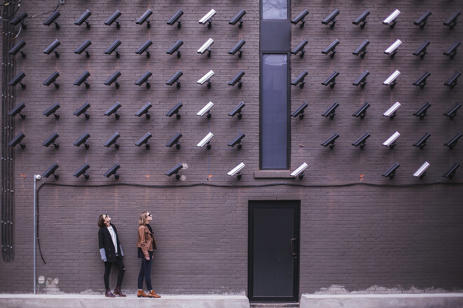 Two people look up at an abundance of CCTV cameras monitoring them.