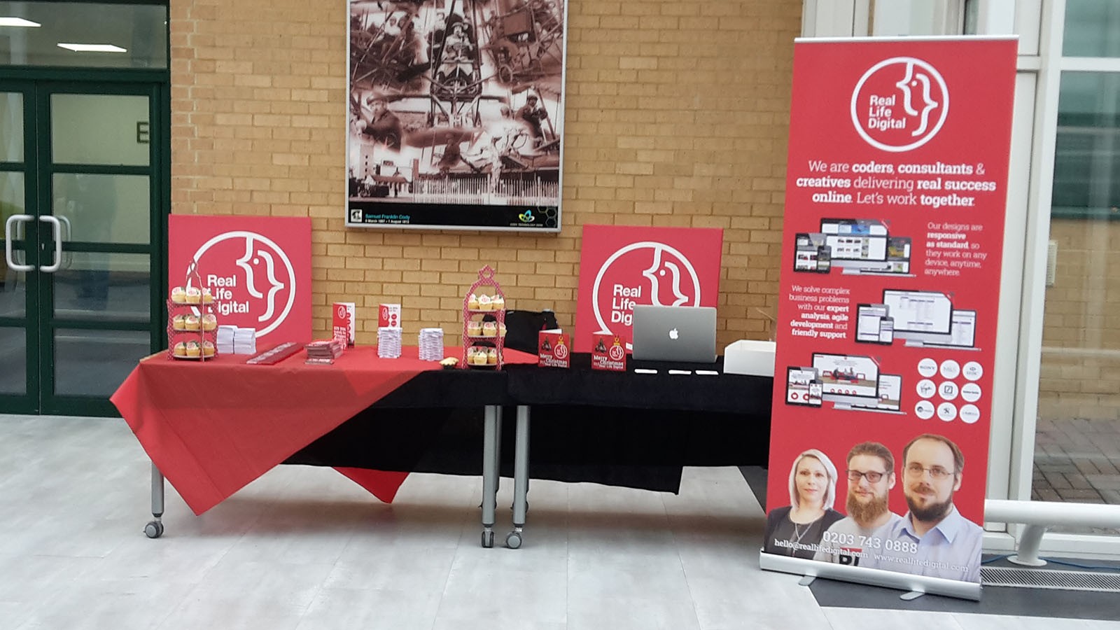 The Real Life Digital stand before the crowds arrived - a long table with giveaways and cupcakes on it. In the background are two large Real Life Digital logos printed on to canvas and to the right is a pop up banner featuring some of Real Life Digital’s work.