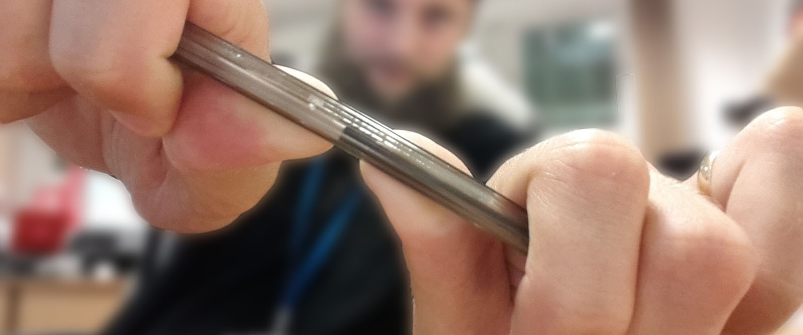 A man is holding a pen up to the camera and is in the process of snapping it in half.