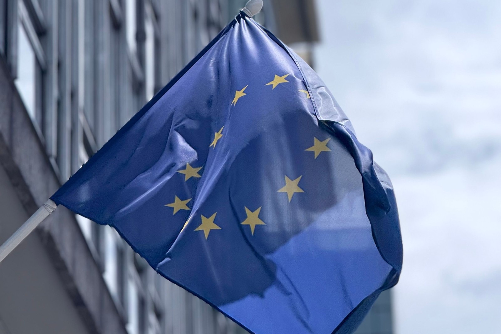 The European Union flag waving outside a modern office building.
