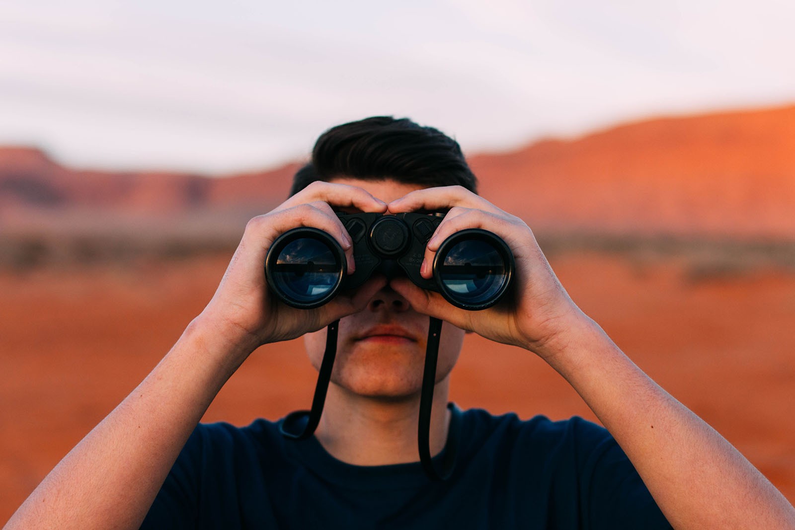 A man looks in to the camera through a pair of binoculars.