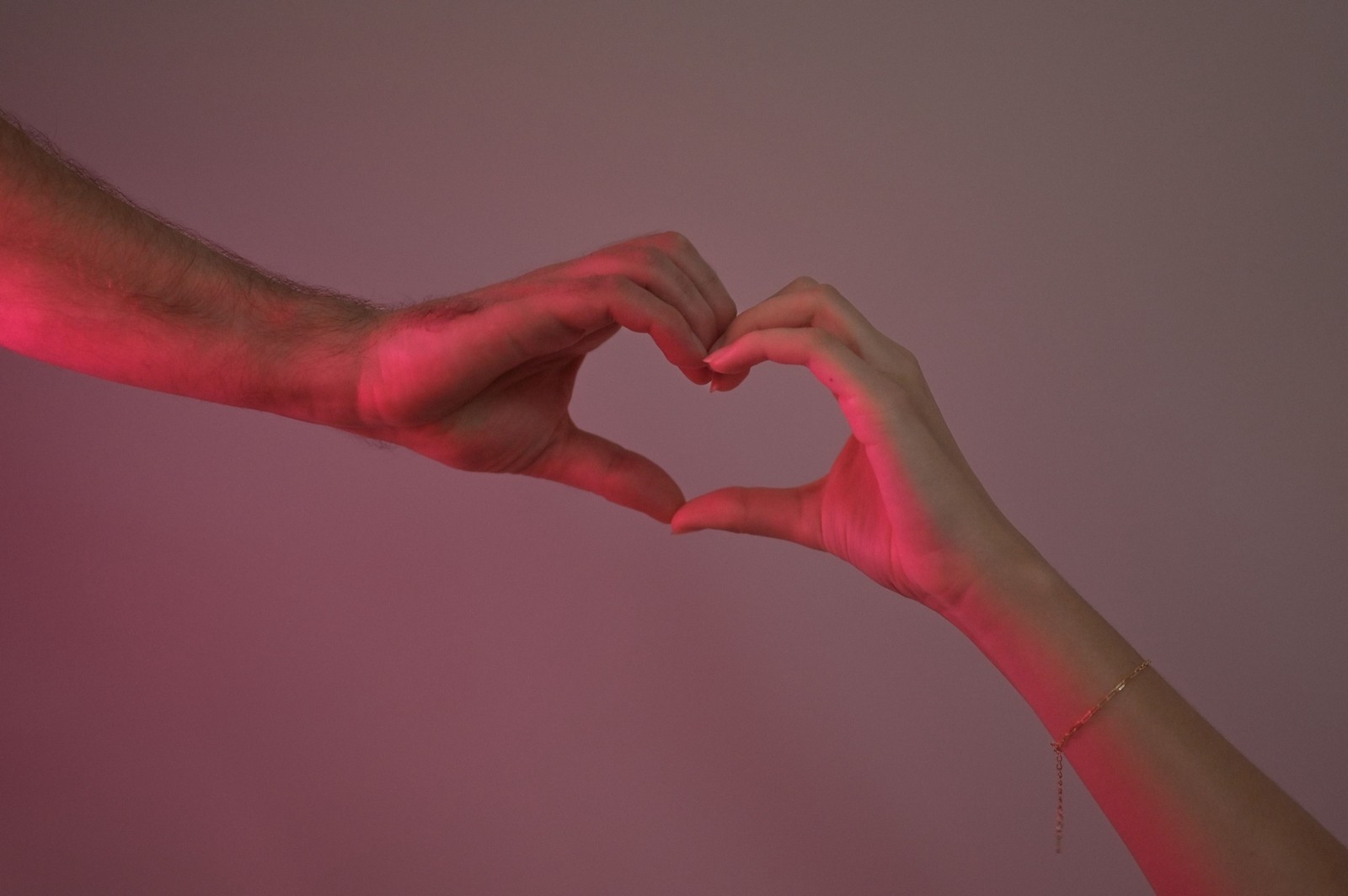 Two hands forming a heart shape against a pink background.