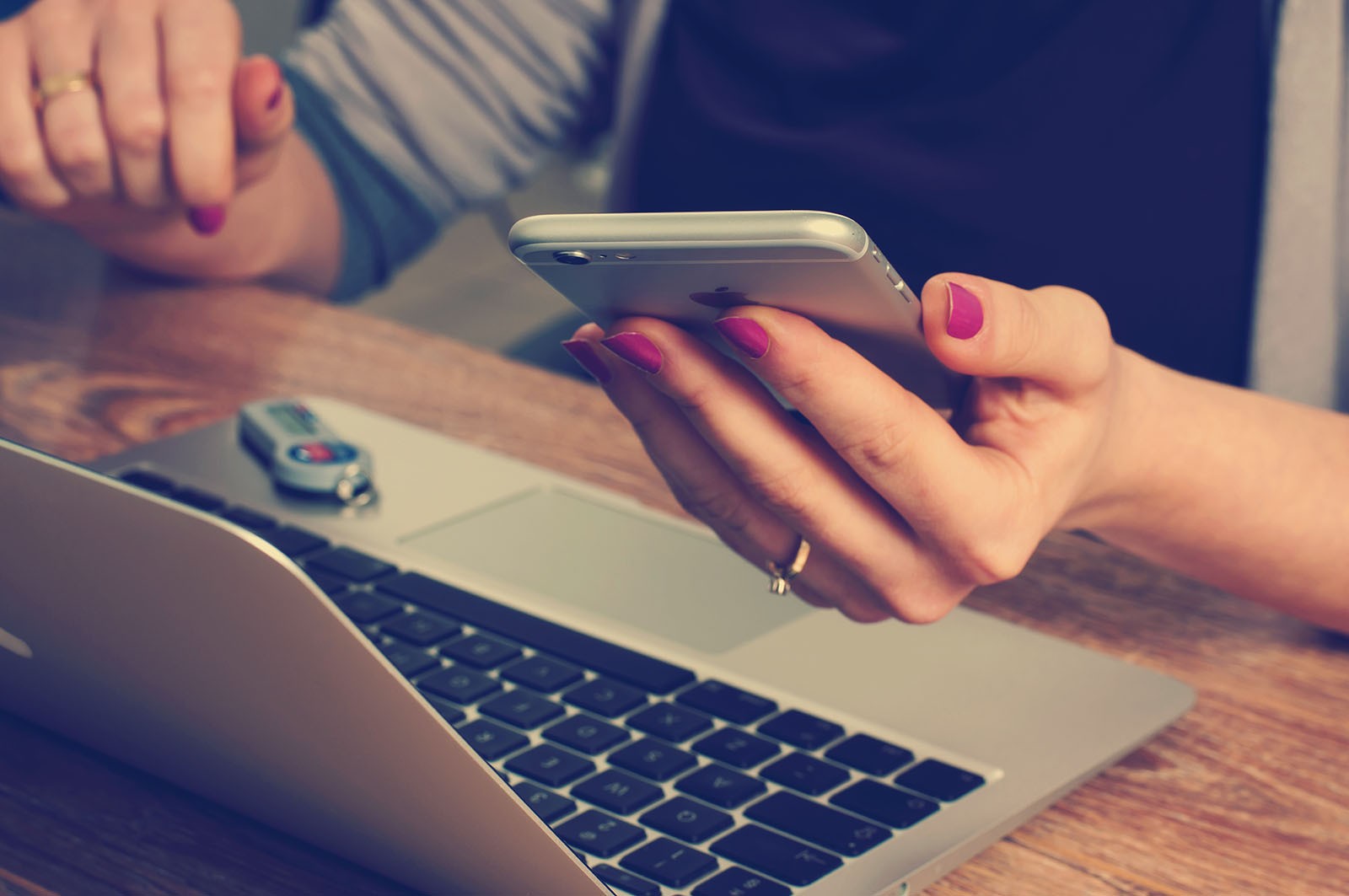 A lady looking on a phone and her MacBook.