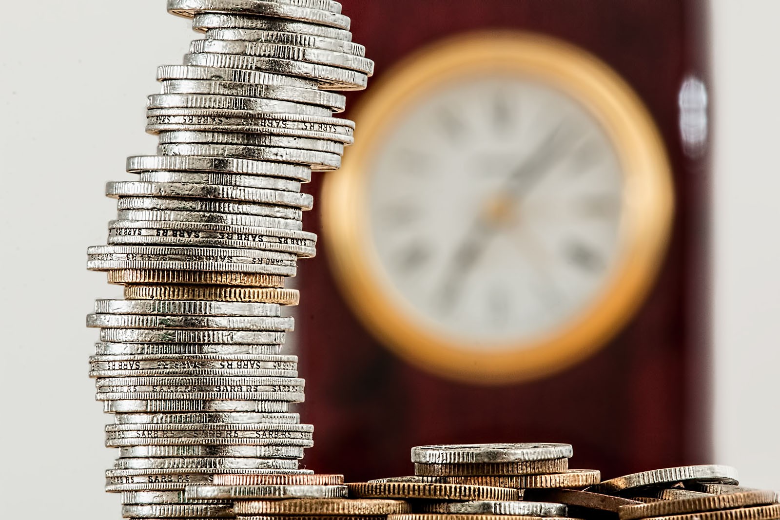 A stack of coins in front of a large (but obscured through blur) wall clock.