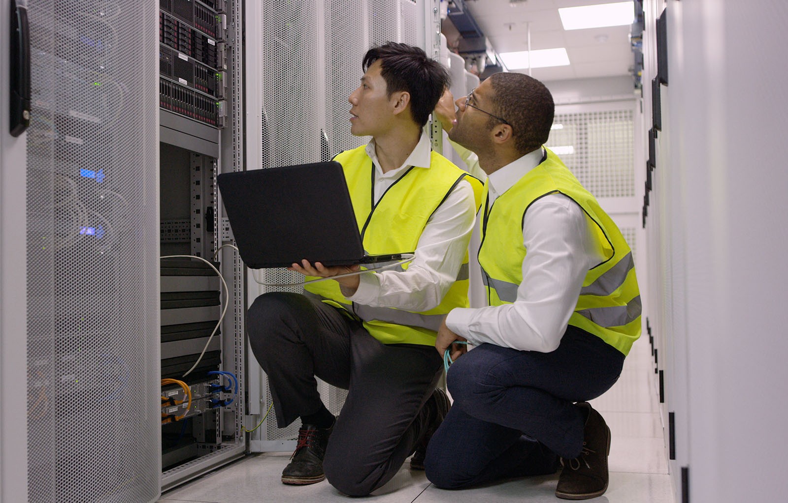 Two engineers knelt by a rack with a laptop performing maintenance.