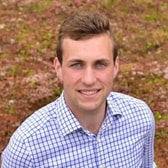 Mark Chambers smiling, with short side-parted hair, wearing a checked shirt, in front of low ground-cover plants.