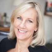 Lexie Gower smiling broadly, with shoulder-length light hair, wearing a dark top.