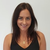 Niki Evans smiling, with long dark hair, wearing a sleeveless top and a pendant necklace.