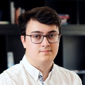 Daniel Johnson with a slight smile, short dark hair and rectangular glasses, wearing a white collared shirt.