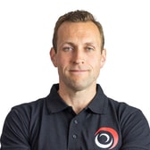 Mark Chambers with a slight smile and short hair, wearing a dark polo shirt with a logo on the chest.