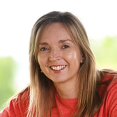 Rosanne Chamberlain smiling, with long straight hair, wearing a light jumper, outdoors.