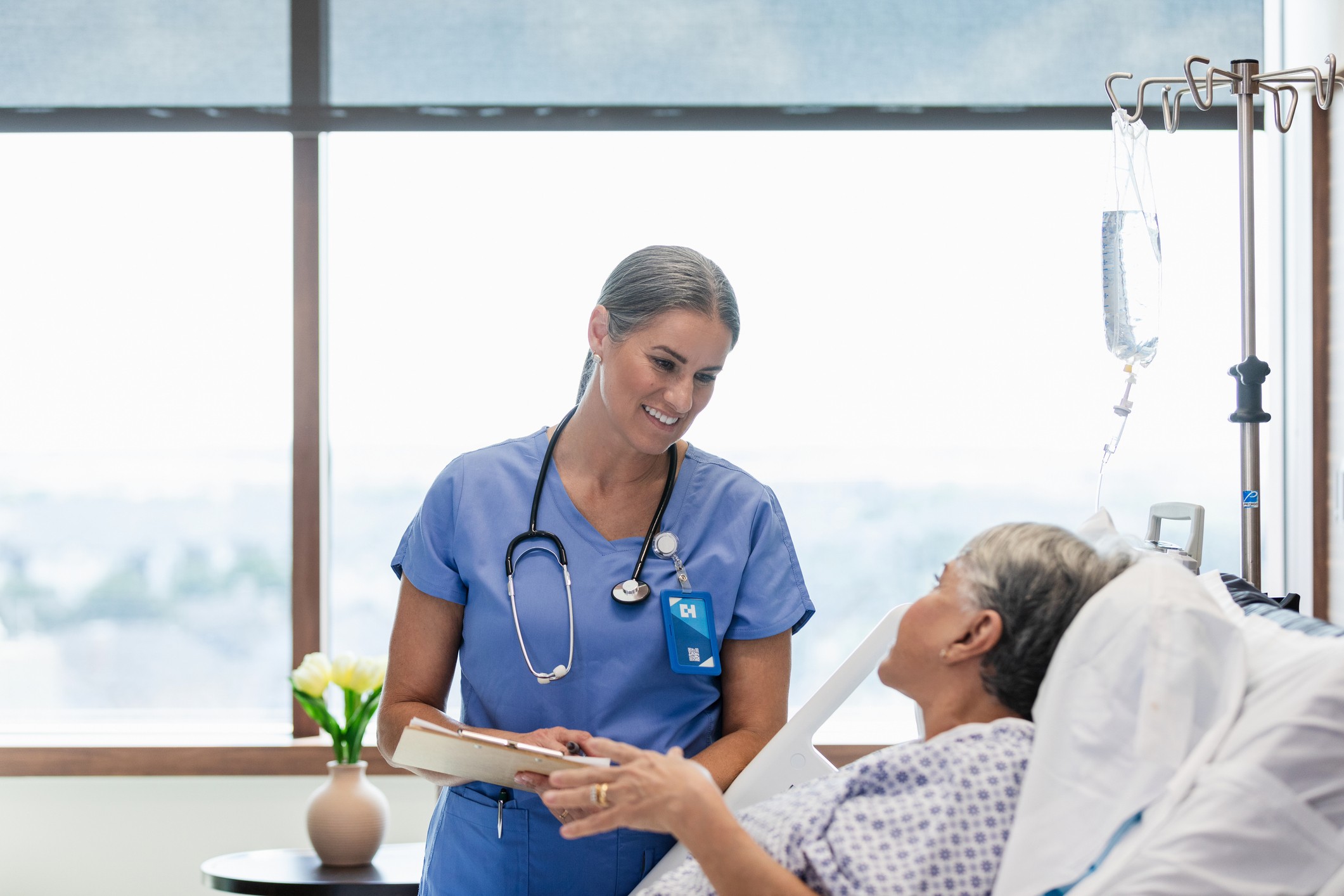A doctor stands by a hospital bed as an older woman talks.