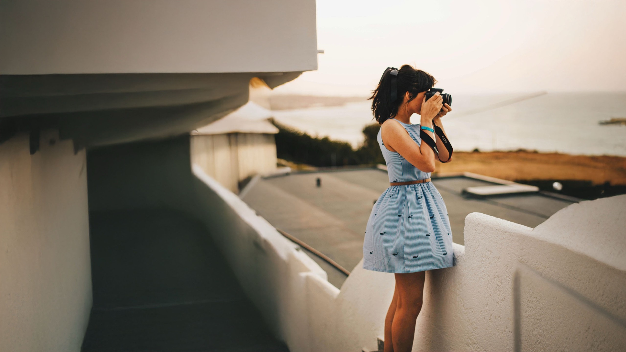A woman photographer wearing a blue sleeveless dress takes a photograph for a free stock photography website.