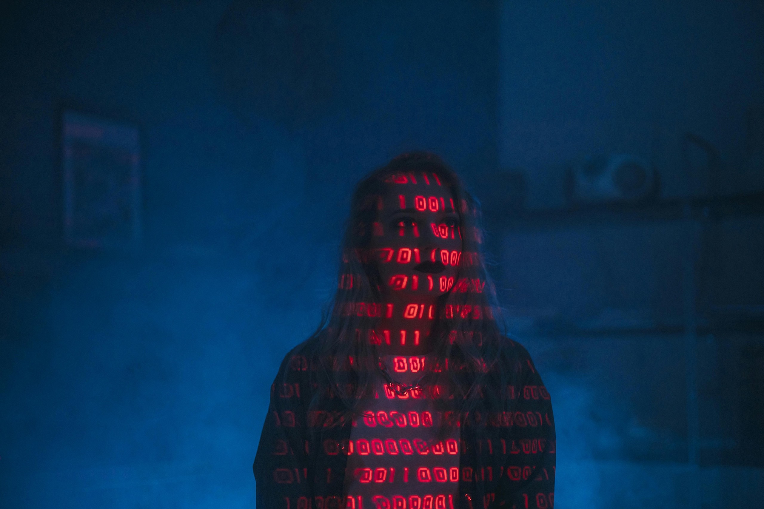 A hacker with red binary code projected on to her face.