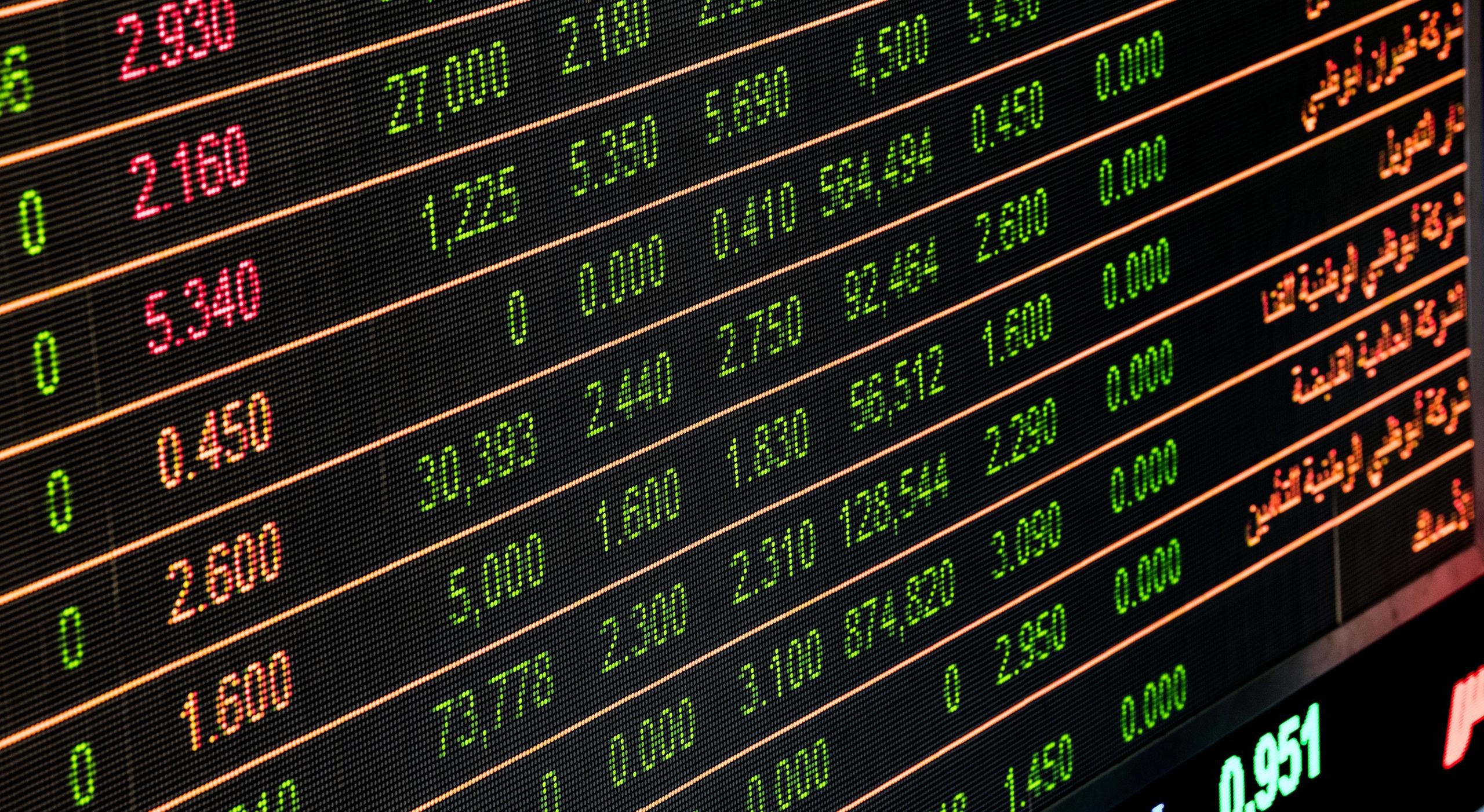 A close-up of an electronic stock market board showing share prices in green and red.