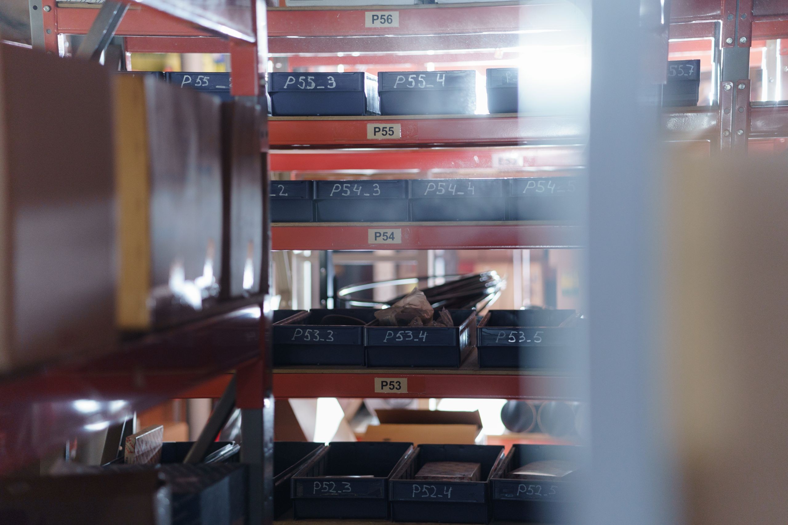 Warehouse shelving with rows of plastic bins, each with a handwritten product code label.